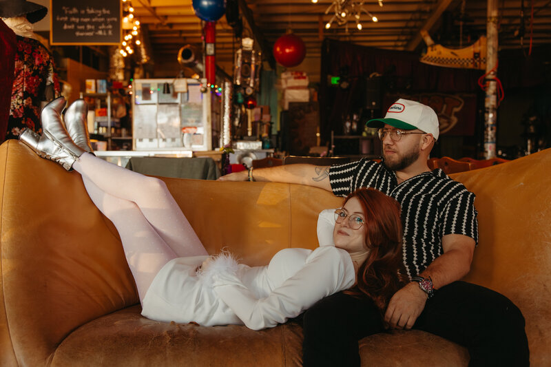 woman lays on orange leather couch with head on mans lap