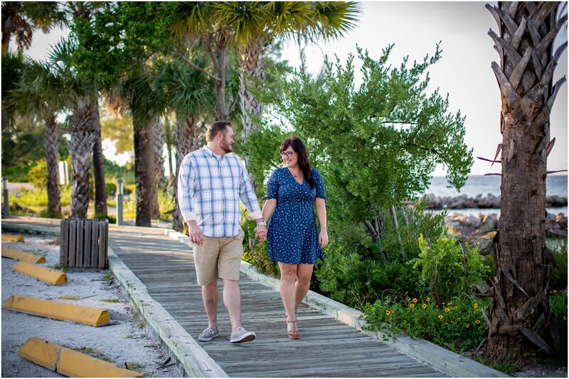 An engaged couple holding hands walking along the boardwalk along Anna Maria Island's city pier