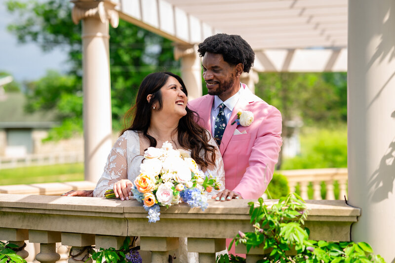 A bride and groom look at one another while the bride's veil floats behind her outdoors