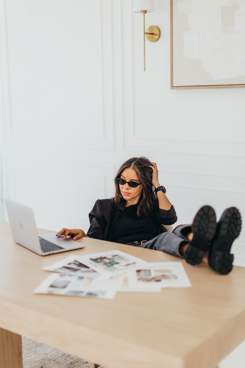 Cool and confident at the desk-legs up, shades on, blazer sharp. Laptop open and brand-colored papers scattered with purpose. Serving boss energy with a creative twist.