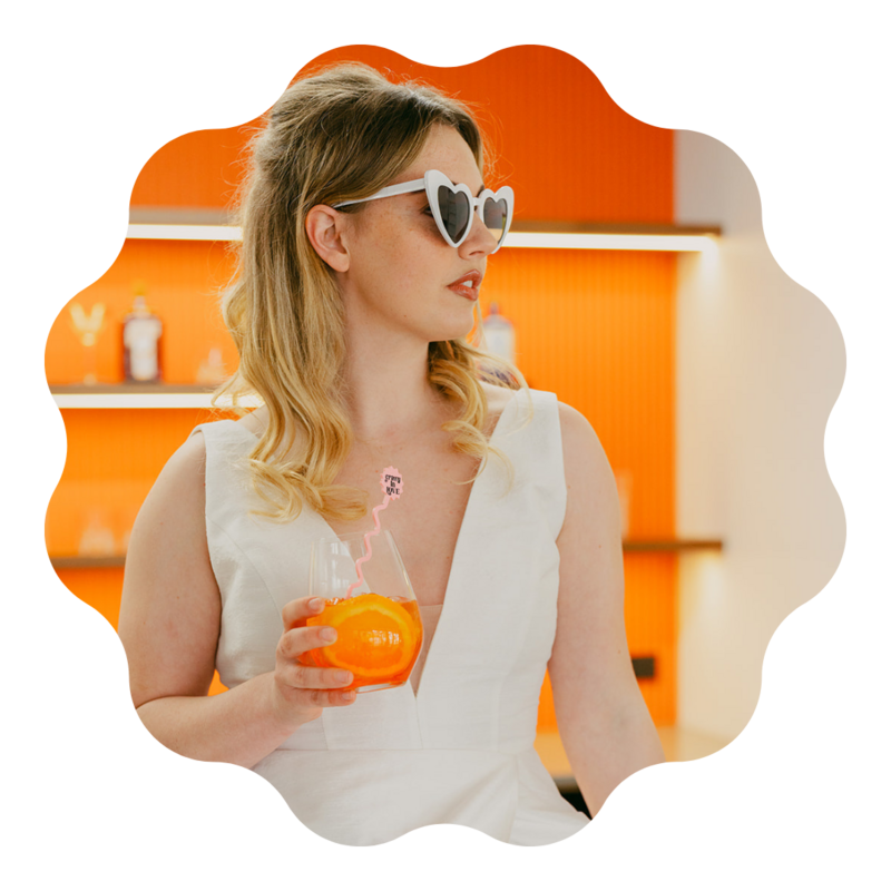 Beautiful bride with heart sunglasses on and an aperol spritz in her hand