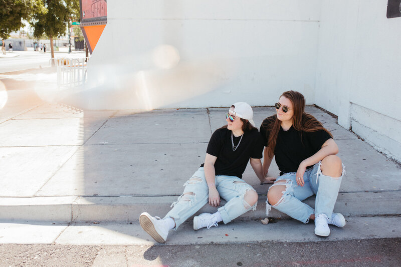 Two people looking off to the side as they sit on a curb.