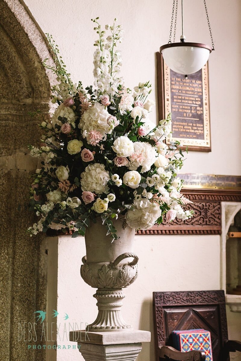 A stone urn of flowers for a church wedding in Cornwall. Filled with hydrangeas, roses and delphiniums