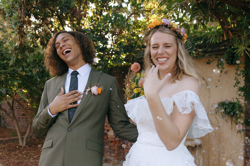 a couple after their California intimate wedding laughing together with bubbles floating around them