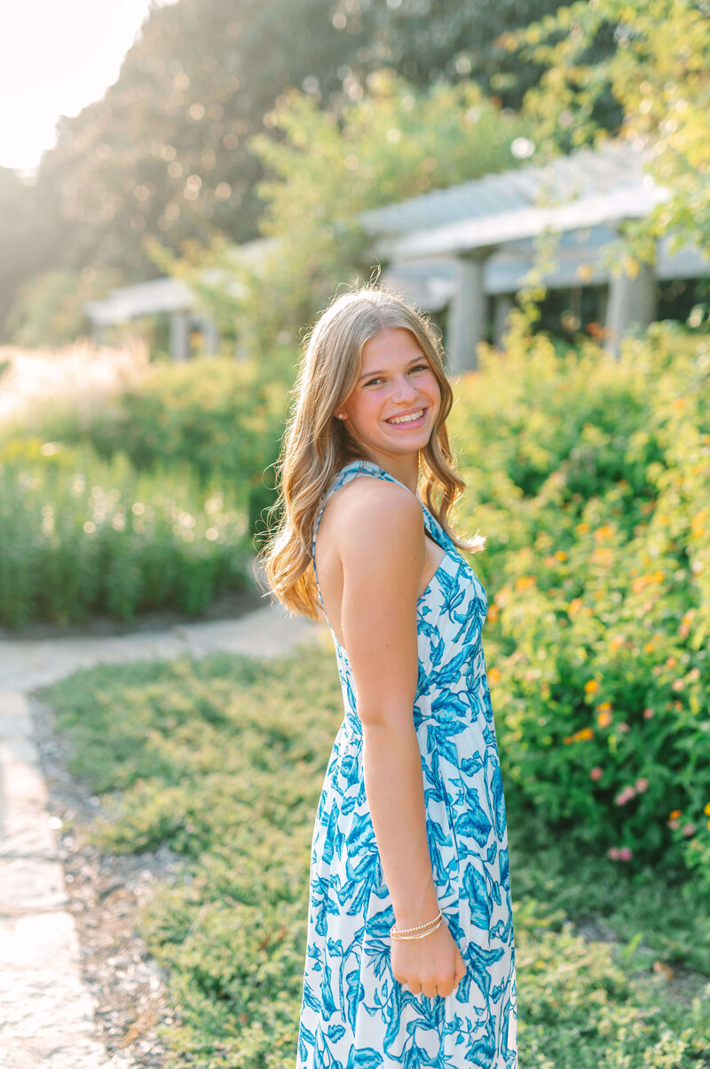 Senior girl smiling in the golden hour light during a senior portrait session with a Virginia wedding photographer, surrounded by lush greenery.
