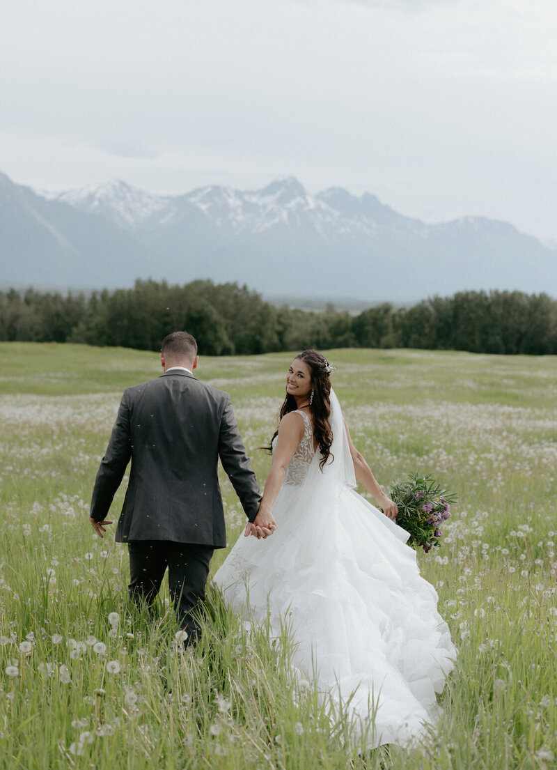 A man and woman holding hands and walking in a field of tall grass.