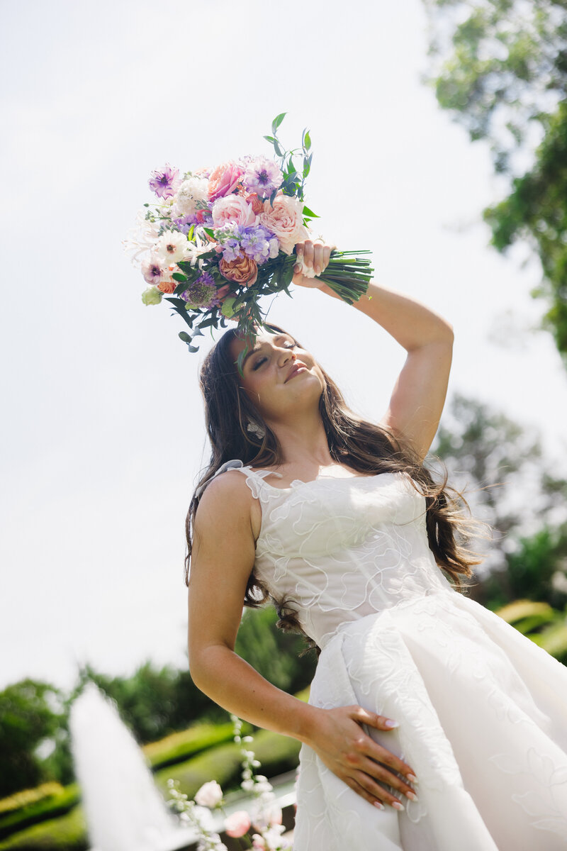 Bride wearing expensive gown holding her bouquet above her face at wedding | Something Borrowed Event Company