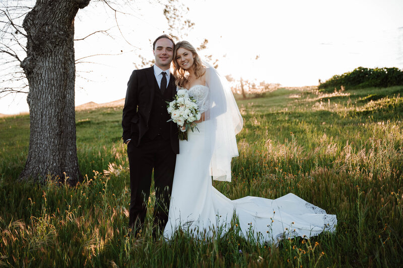 Bride and groom pose in green field with bouquet
