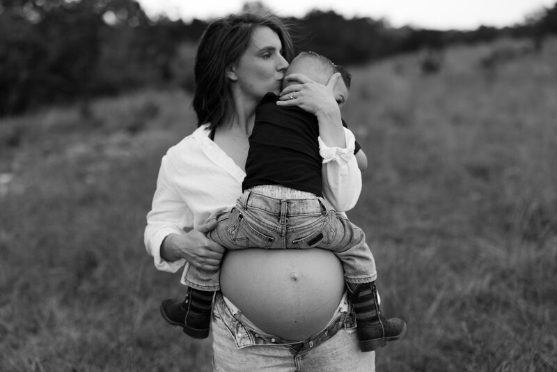 A mama holding her son on her pregnant belly while kissing the side of his head in Austin. 
