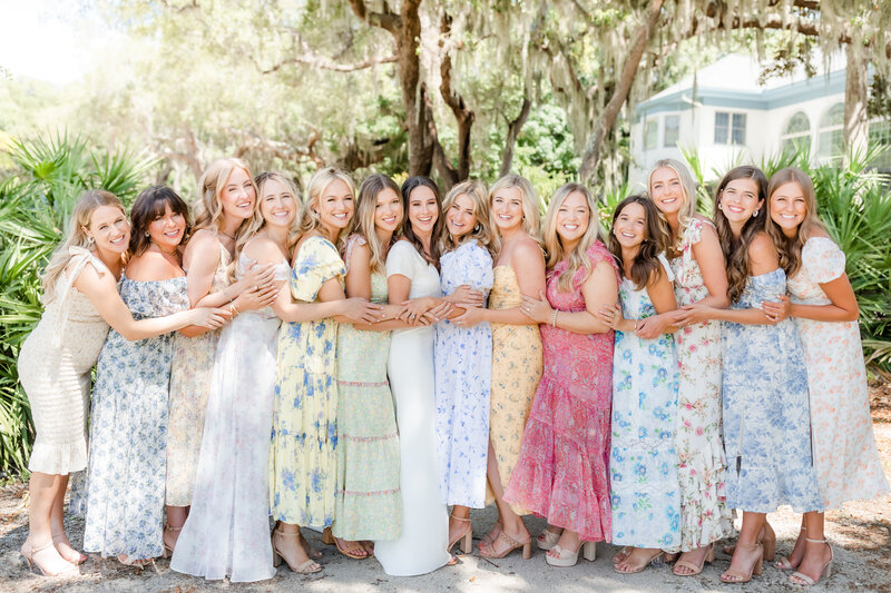 Bride in a hug with her bridesmaids dressed in a mix of floral gowns