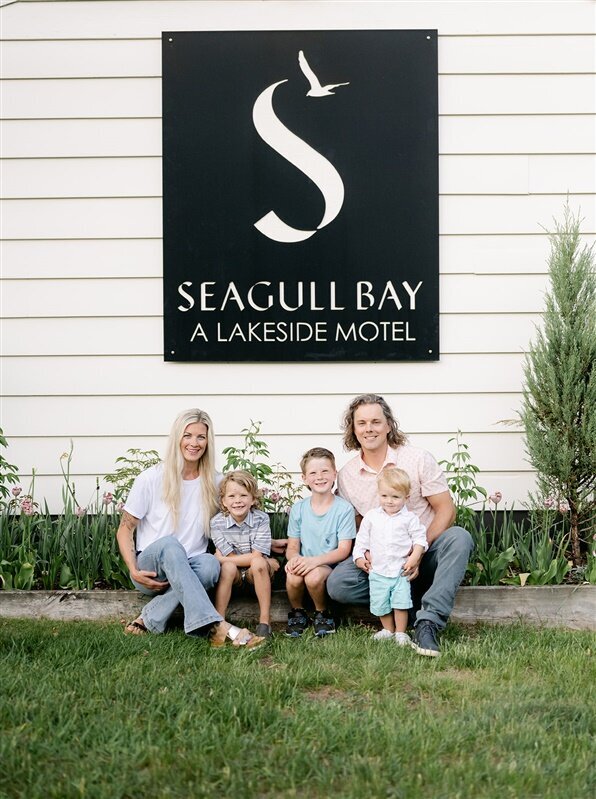 Seagull Bay Motel owners Mollie and Isaac Carrier and sons Axel, Ridge, and Banks sit on the lawn in front of Seagull Bay Motel sign