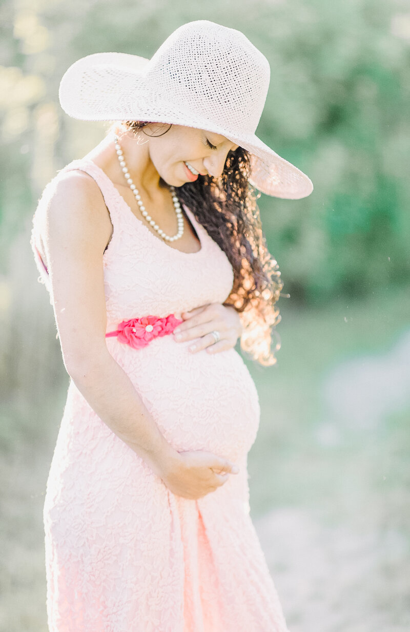 Pregnant mother in pink dress and pink hat glowing in warm light