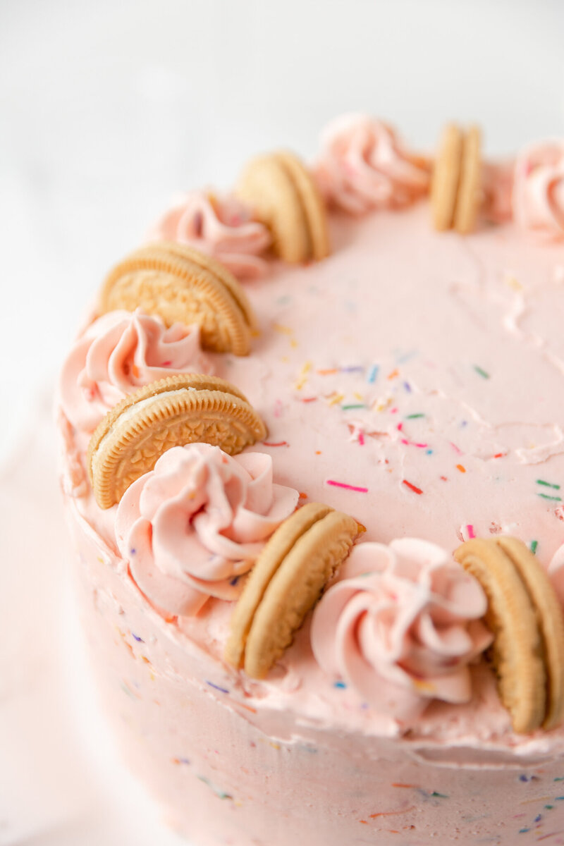close up of a cake decorated with pink frosting, golden Oreos, and sprinkles
