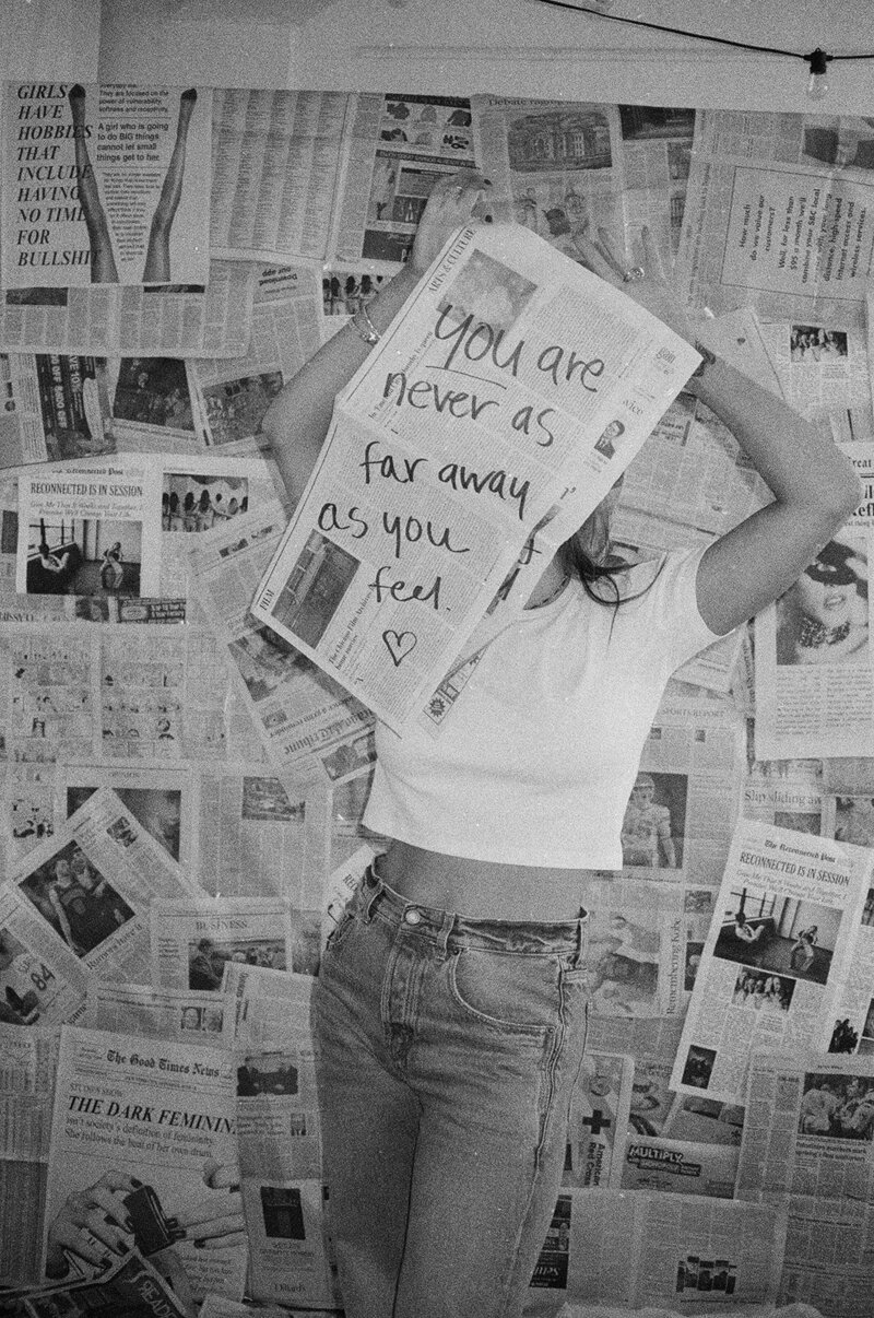 A woman sitting on the beach holding up a newspaper that says Reconnected is in session.