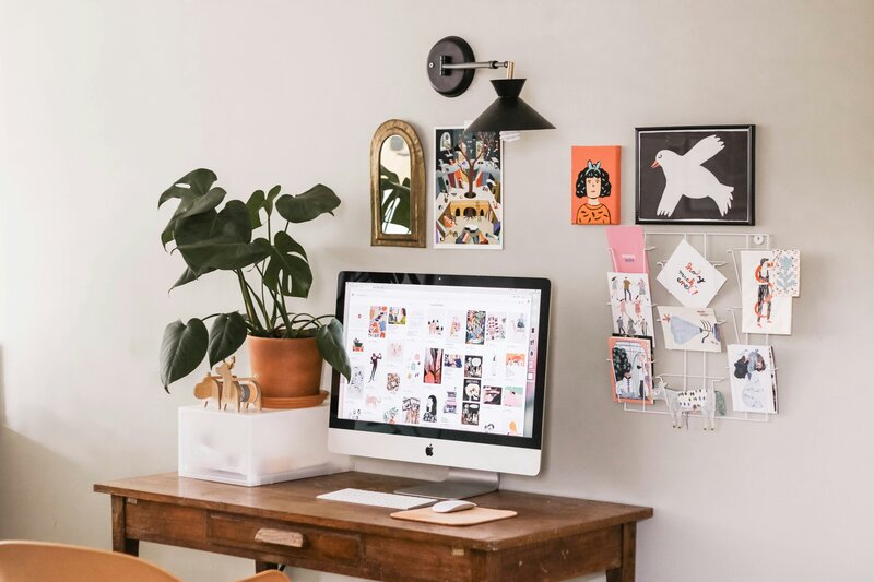 computer on desk with plant and pictures on the wall 
