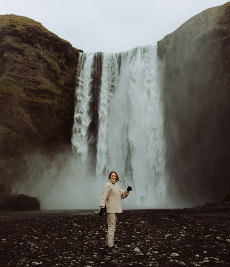 en glad kvinnlig fotograf dansar framför ett vattenfall på island
