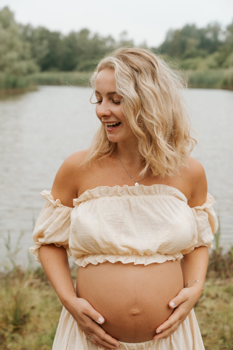 Zwangere vrouw die lacht en buik toekijkt tijdens een zwangerschapsshoot in Antwerpen.