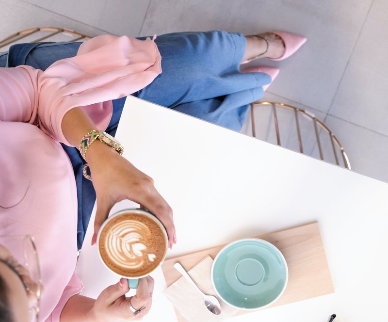 Woman in pink shirt sitting at a table holding cup of coffee