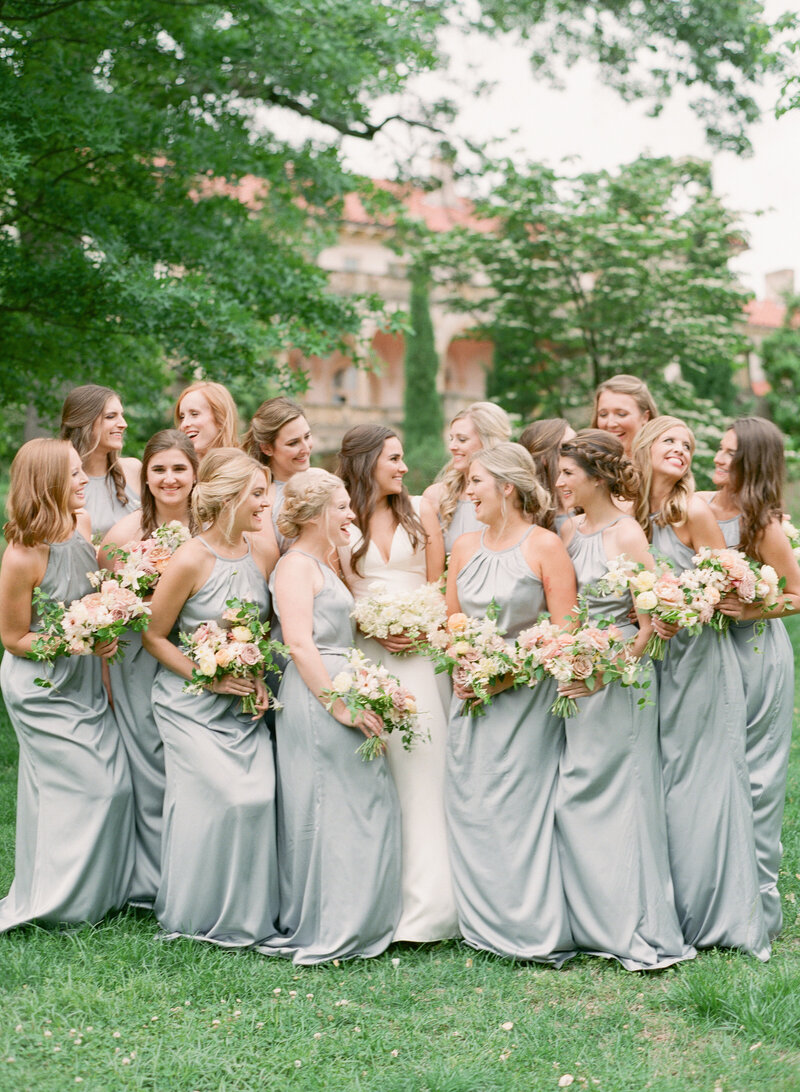 A group of a bride and her bridesmaids laugh together while holding Anthousai bouquets.