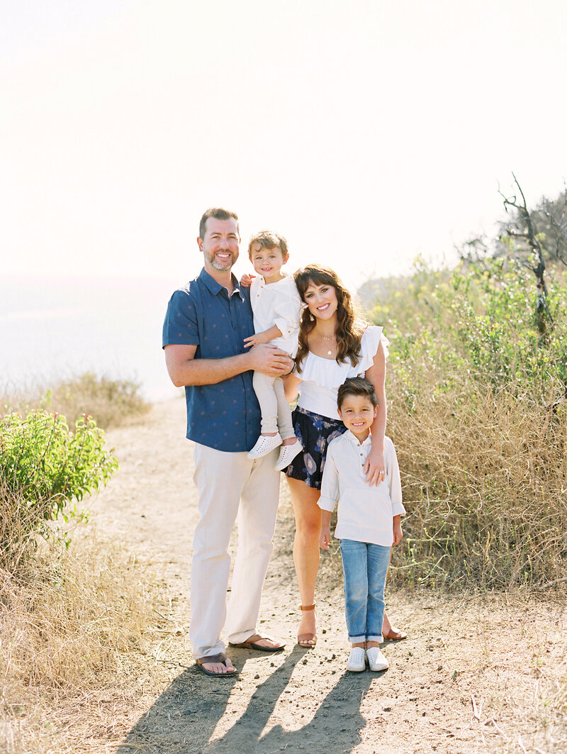 A family on the cliffs in Malibu smiling during their family photo session with Daniele Rose