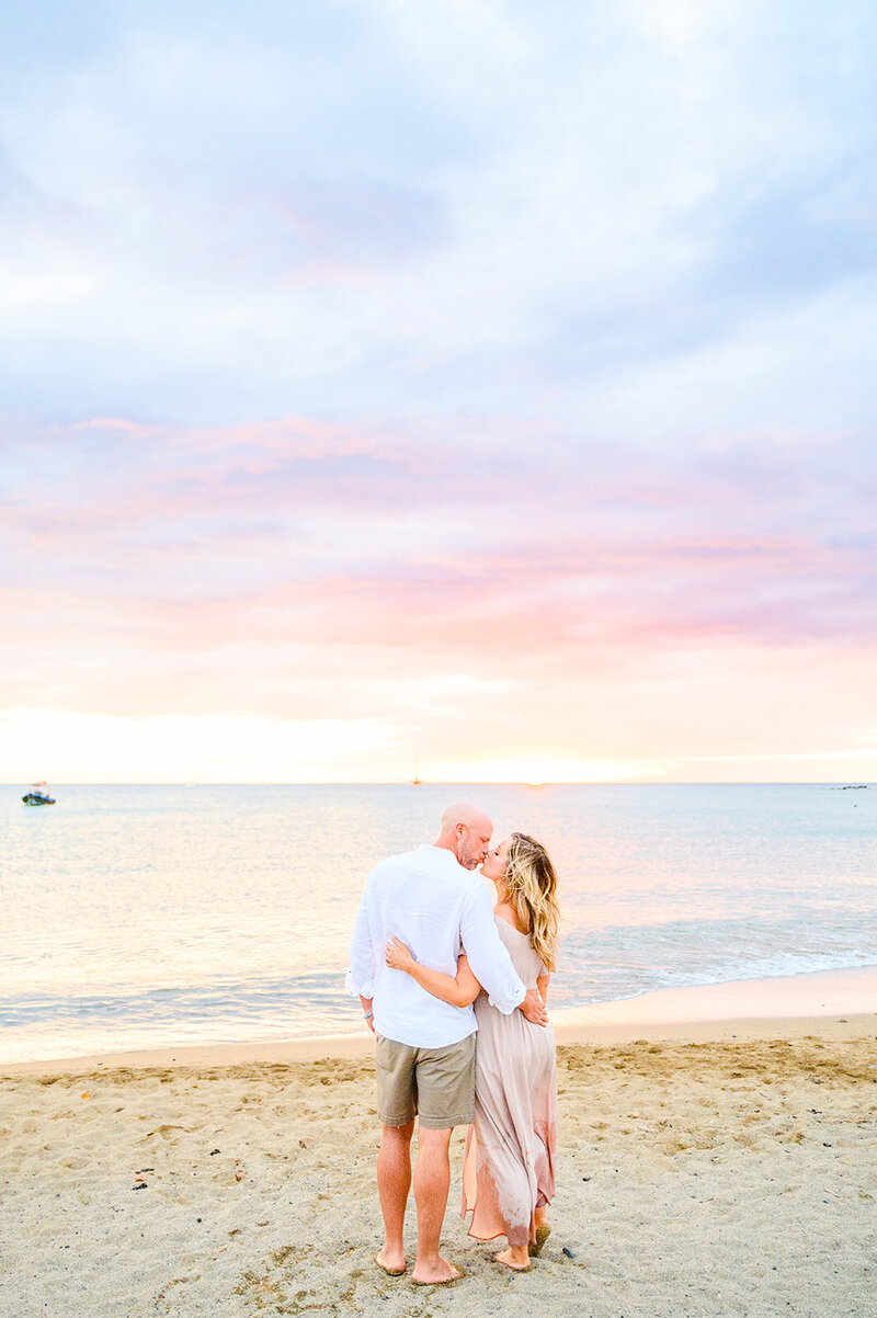 couple kissing on the sand at sunset with colorful pink  soft clouds