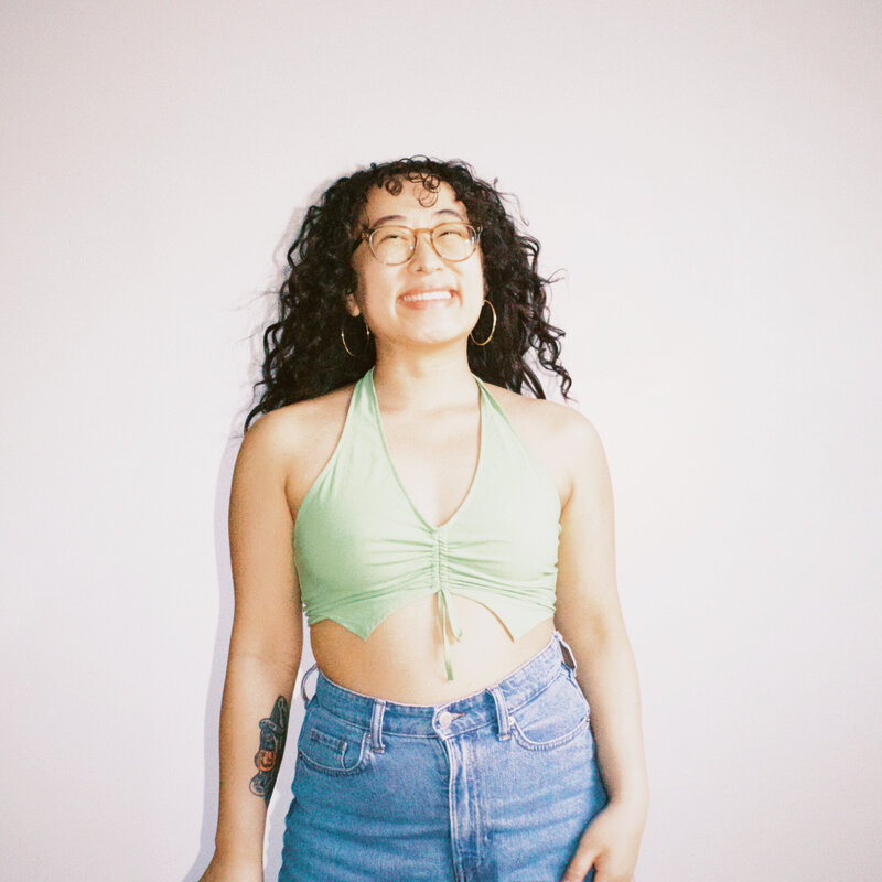 Asian woman smiling with curly hair and light green crop halter top and blue jeans