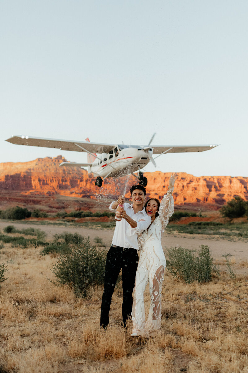 Bride and groom standing on a red rock arch in Moab at sunrise.