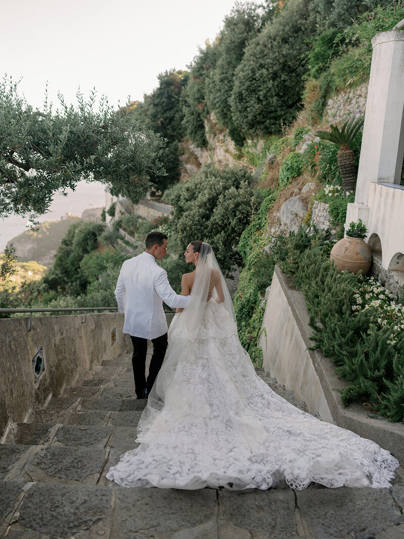 Bride in Monique Lhuillier stands on balcony at her wedding in Ravello Italy