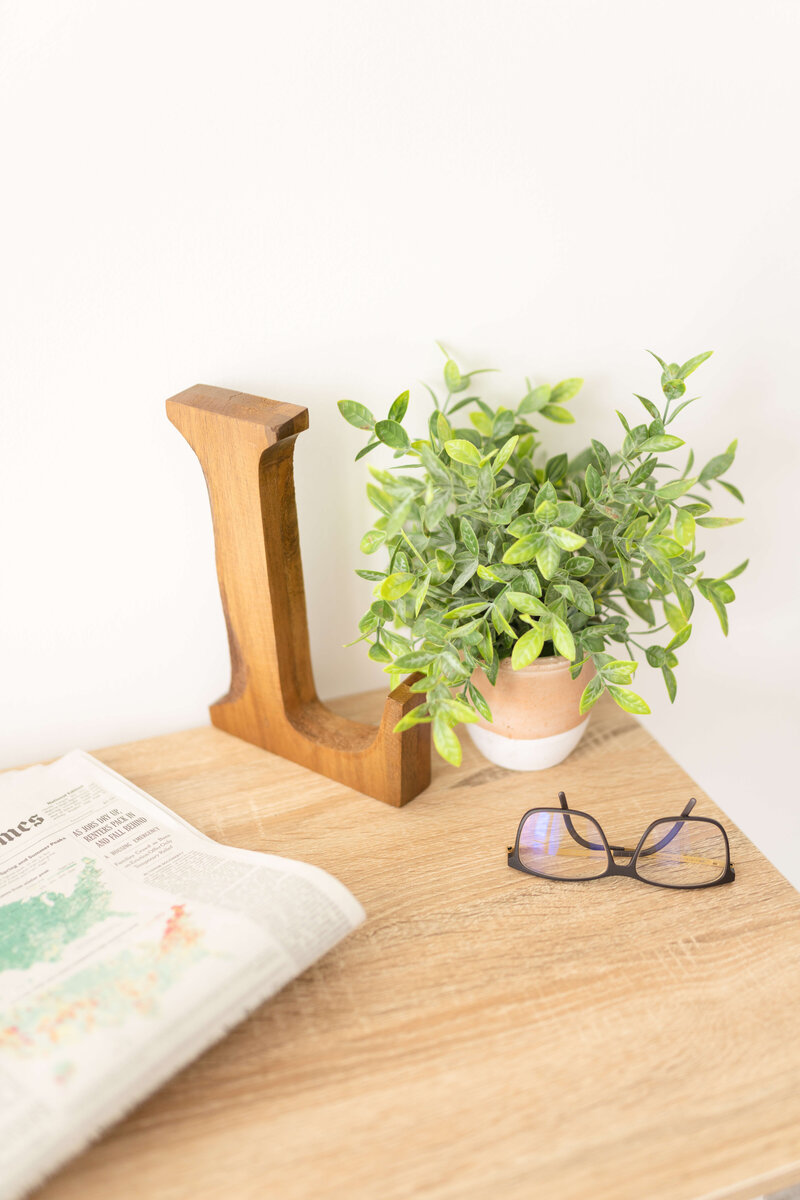 Wooden "L", plant, glasses and newspaper on desk.