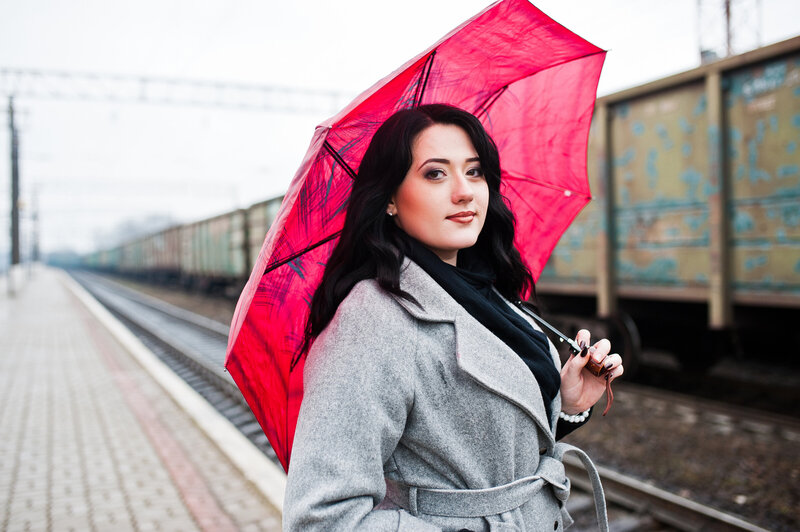 Author holding red umbrella in grey tweed jacket, dark brown hair down