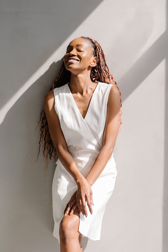 Smiling woman in a white dress leaning against a wall