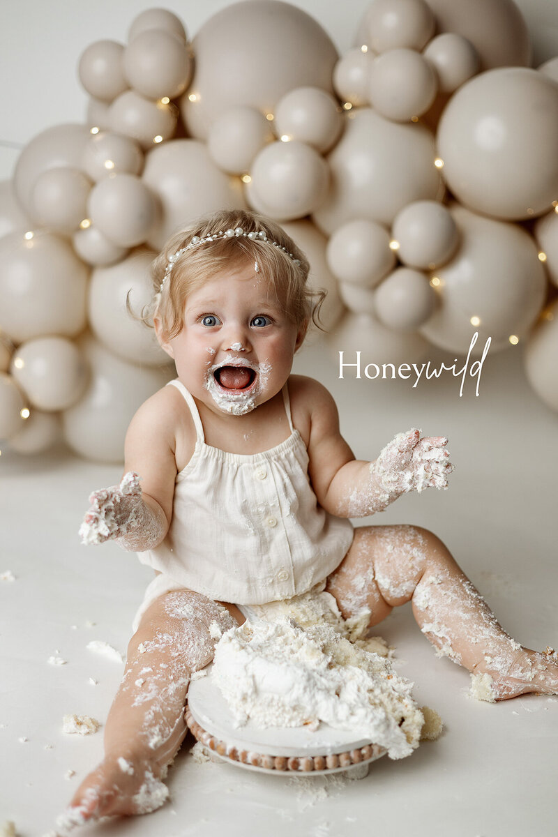Milestone and cake smash photography in Grand Rapids – toddler girl covered in frosting in studio session
