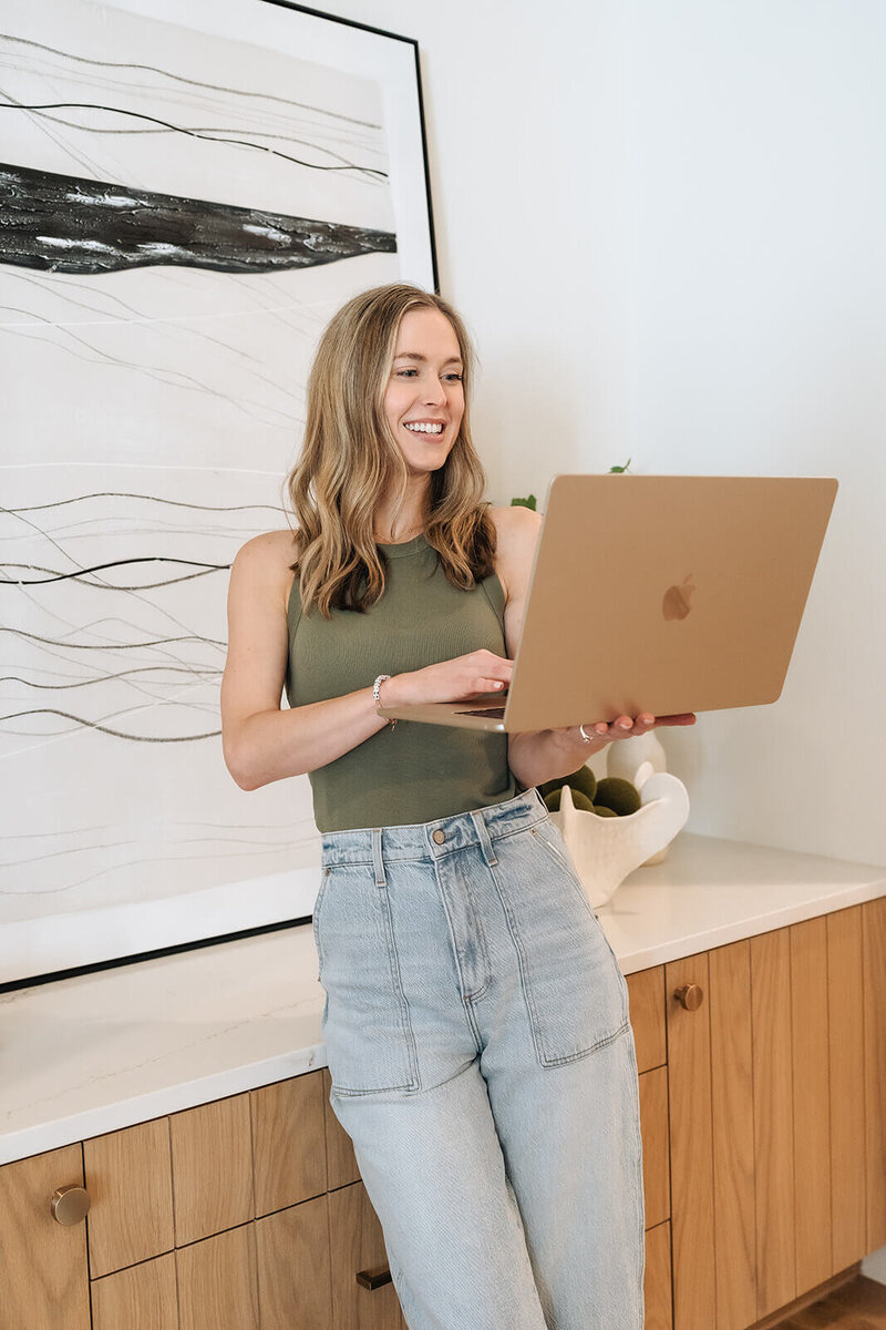 Erica Taylor smiling while using her laptop—offering supportive wellness coaching and a personal connection for moms considering a reset