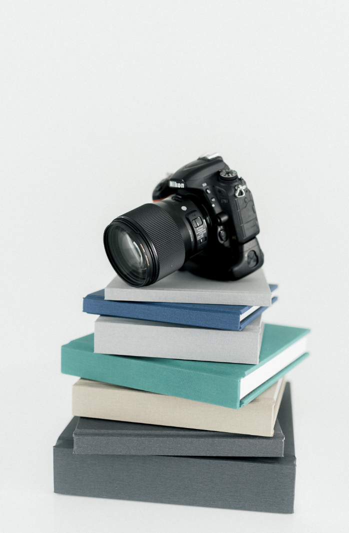 A black camera sits on a stack of blue and gray wedding albums.
