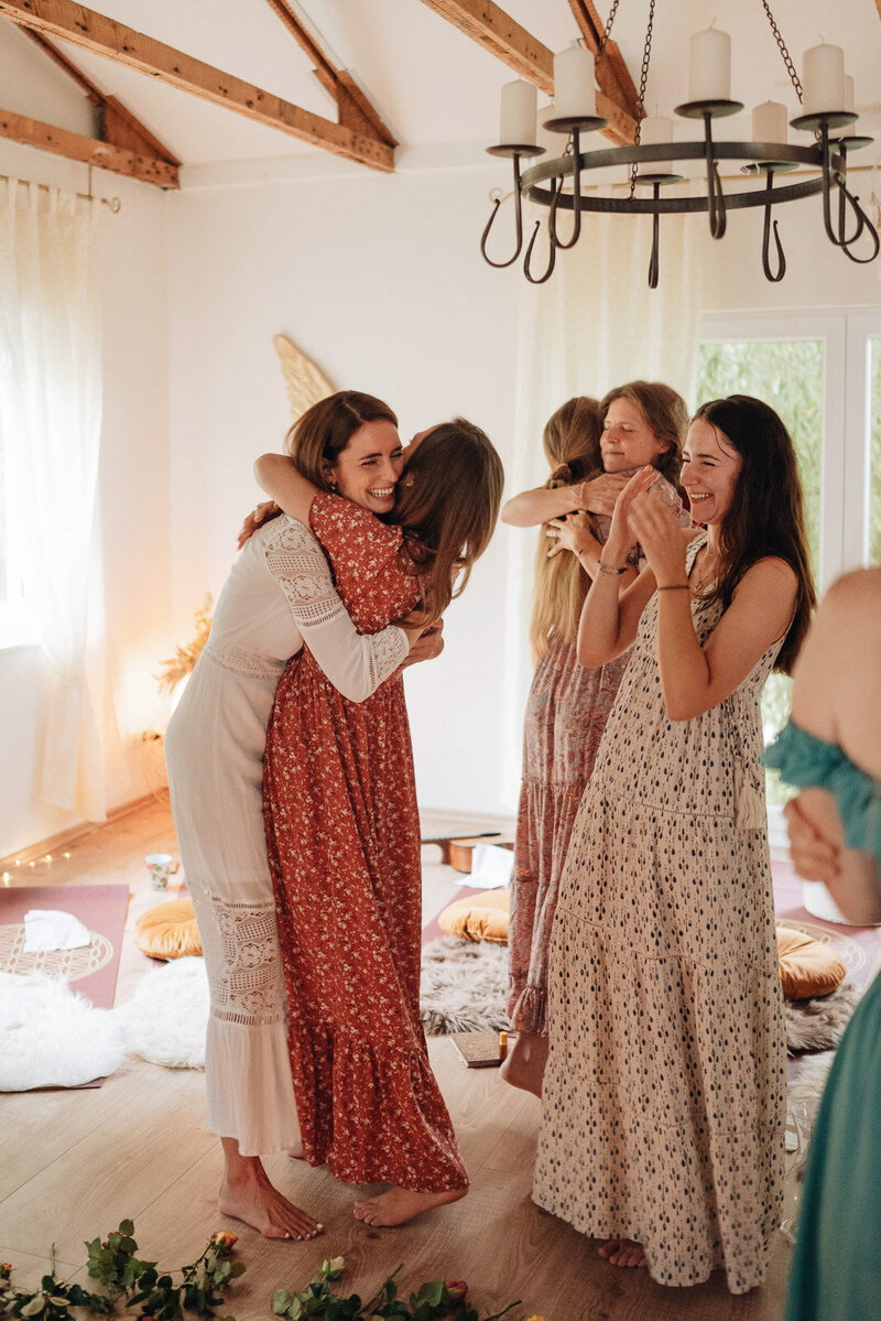 Frauen in langen bunten Kleidern umarmen sich bei einem Retreat im Landhaus Morgan