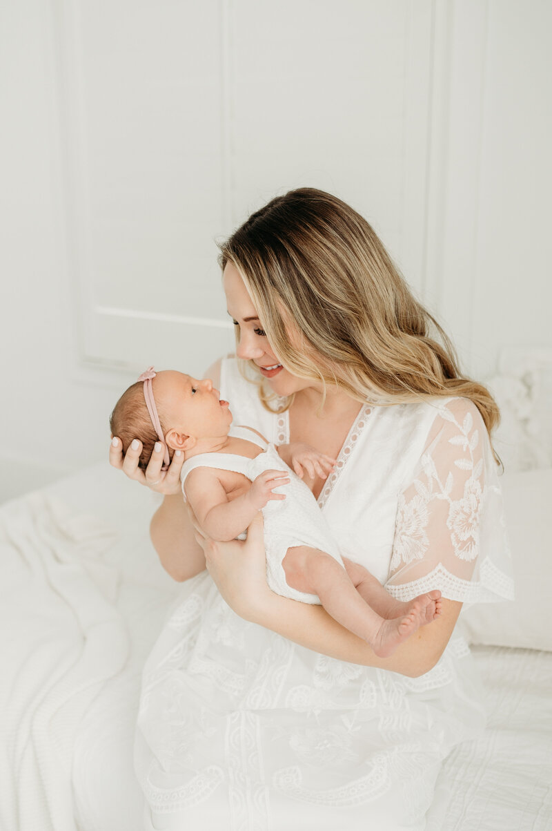 A newborn baby is laying on the tummy with hand under her head with a white blanket over her body. She is showing a gentle smile during her newborn session in Atlanta
