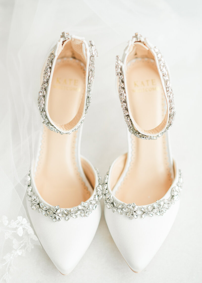 A detail shot of a bride's white and bejeweled wedding shoes.