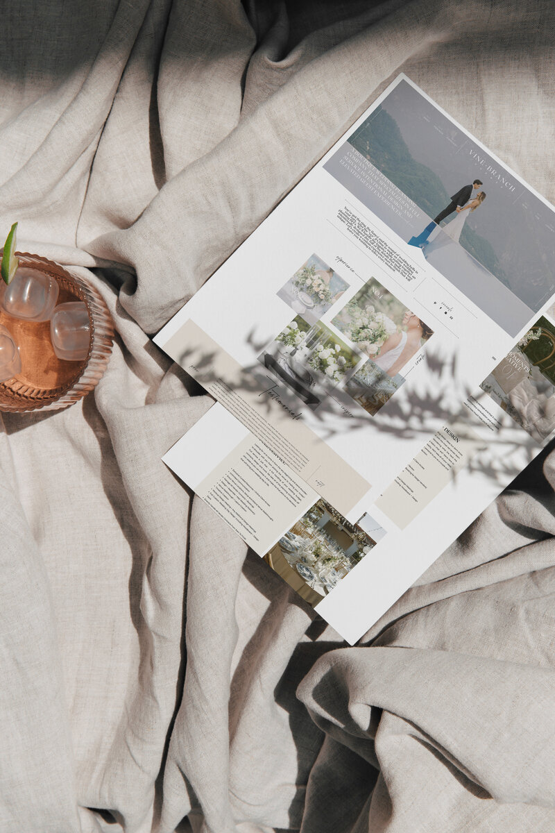 Aerial view of a wedding magazine page placed on a beige fabric with a small bowl containing ice and a drink to the left. The magazine features images of wedding themes and information, perfect for inspiring your next event as you browse through our website design services for small business.