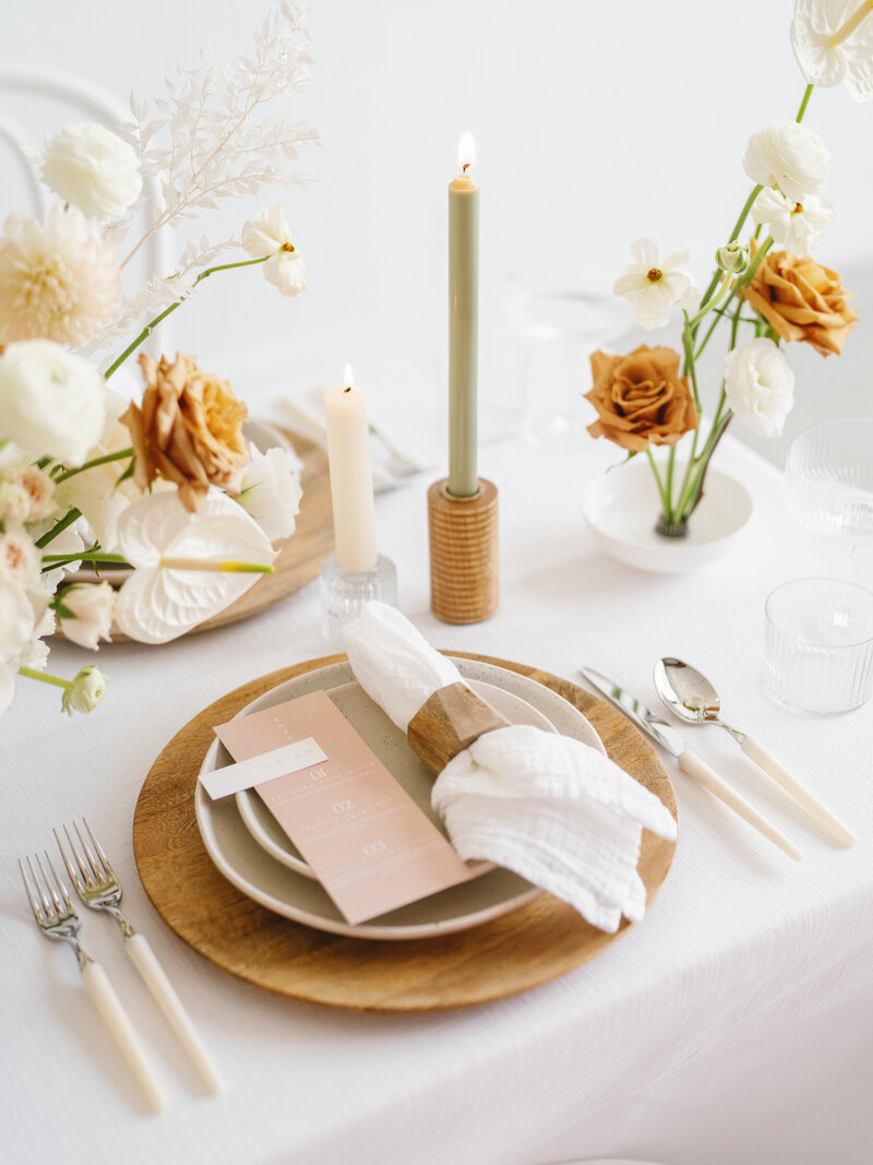 Elegant wedding tablescape featuring modern stationery, neutral-toned florals, taper candles, and a wood charger, styled by Austin wedding planner Eventive Designs.