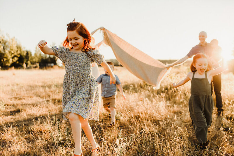 A family plays joyfully together in an open field at their photo session with Vancouver Washington Photographer