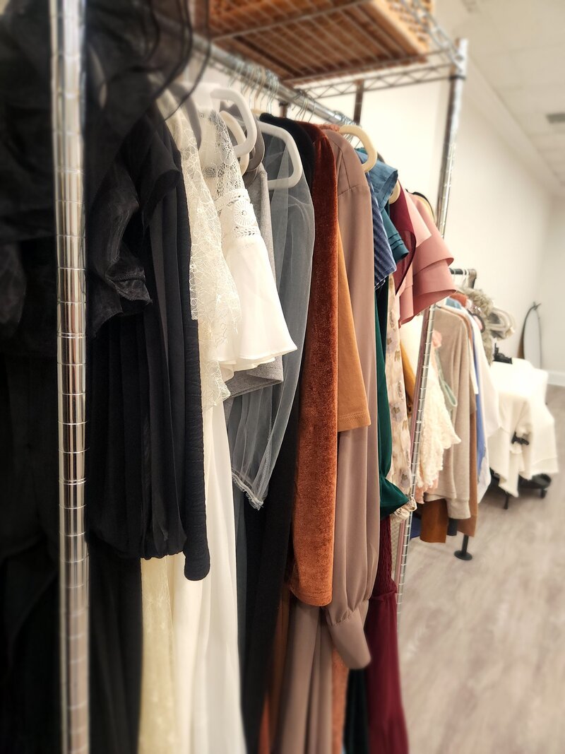 Gowns on velvet hangers hanging on chrome clothing rack in order by color