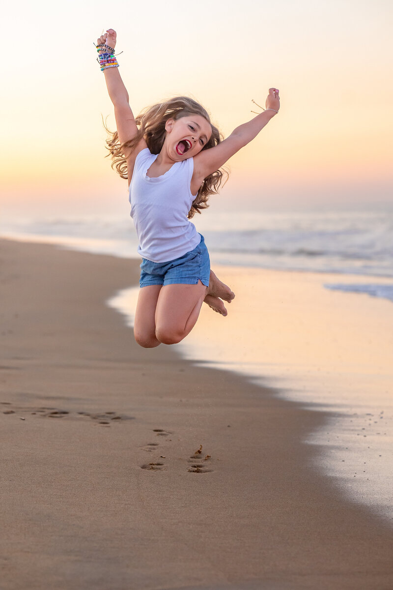 Joyful moment captured by Brooke Tucker as a young girl jumps with excitement on the beach during a candid, playful session in Virginia