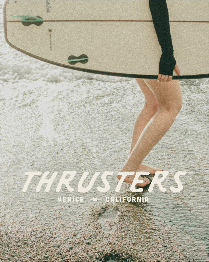 photo of a female surfer holding a surfboard with her feet in the sand and a logo for Thrusters Surf Shop