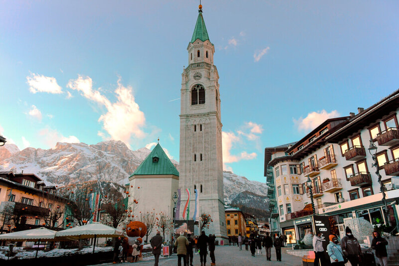 Cortina d' Ampezzo town square with a huge bell tower and snowy mountains in the background