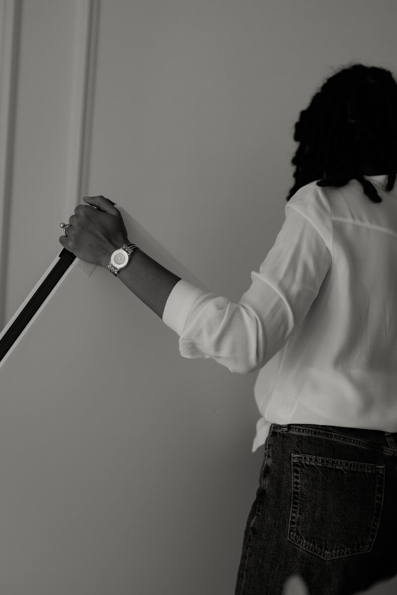 Black and white photo of a Black woman photographer actively working in her Fort Worth studio, moving around equipment. The image showcases her professional environment and dynamic work style.