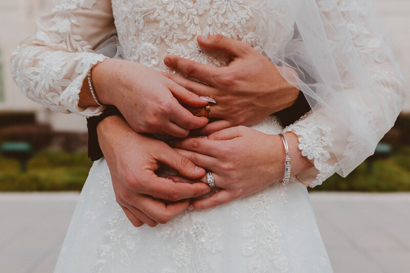 Close-up of the bride and groom embracing, with the groom’s hands gently wrapped around the bride’s waist, showcasing the lace details of the wedding dress during their wedding at the LDS Houston Temple in Texas.