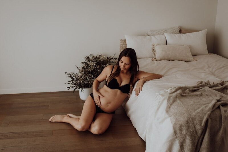 Zwangere mama zittend naast bed in studio tijdens zwangerschapsshoot.