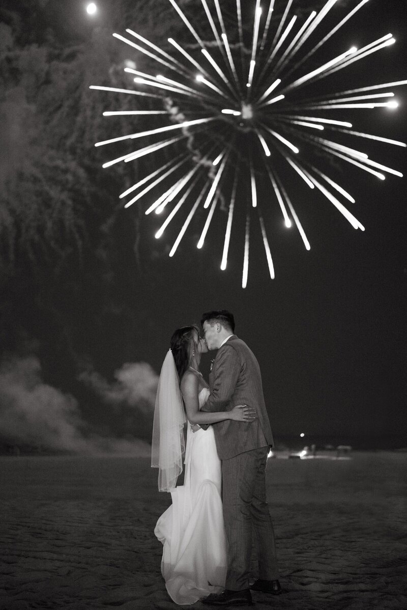 Romantic beach wedding kiss under fireworks at Hotel del Coronado, designed by Thater Made, a luxury wedding and event producer in San Diego, CA.