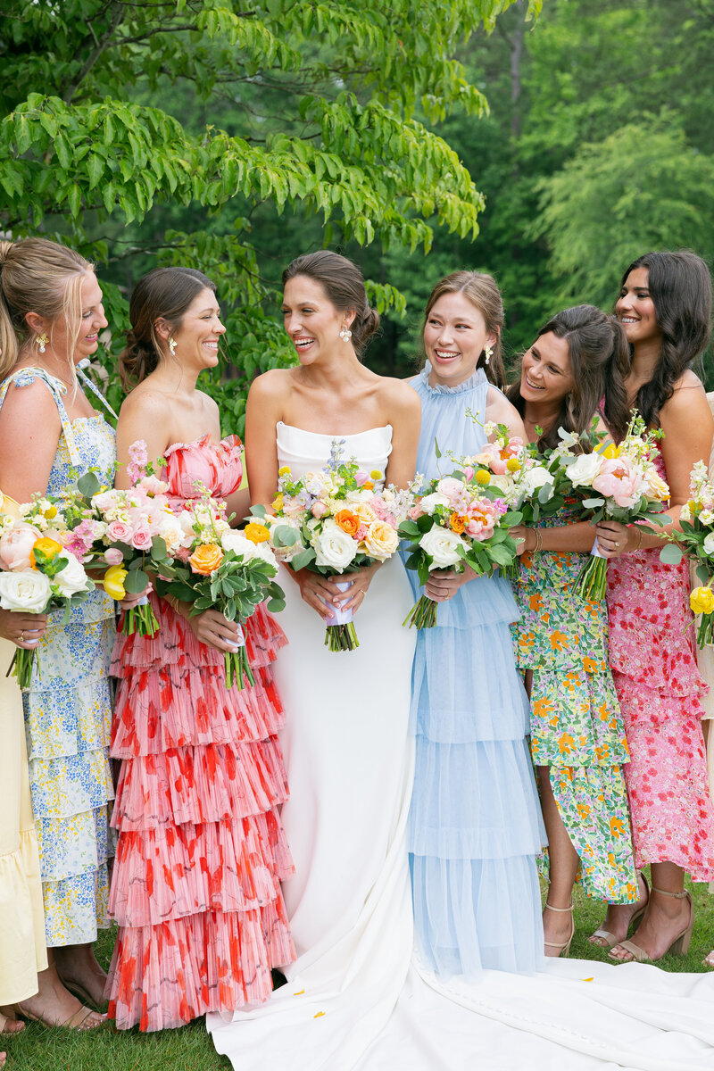 Girls in long dresses smiling at one another with bouquets