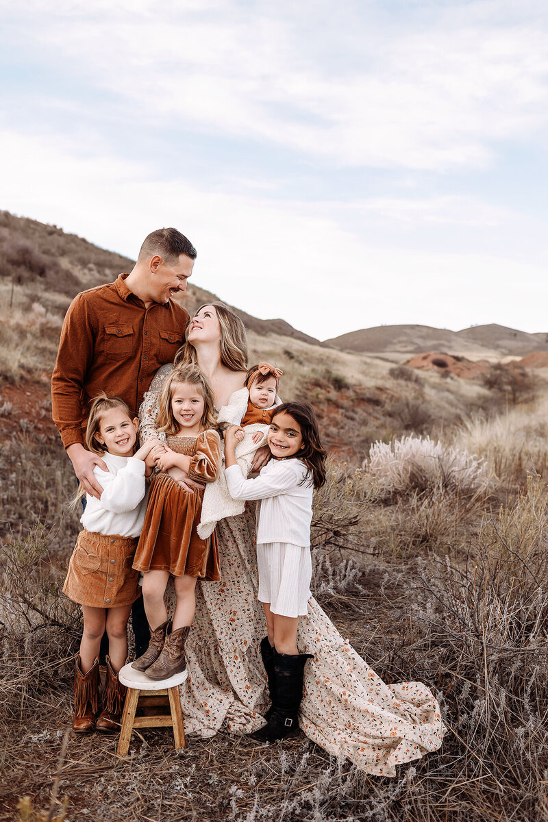 family of five stands against colorado mountains holding moms baby bump for photos at sunset with denver photographer